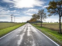 an empty road runs through a grassy plain area and with power lines in the background