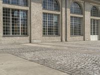 a brick pathway leading to a big building with multiple windows and glass doors and a red fire hydrant