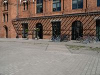 a very wide and empty brick sidewalk next to many bicycles in the background, a building with multiple windows