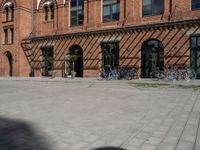 a very wide and empty brick sidewalk next to many bicycles in the background, a building with multiple windows