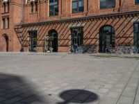 a very wide and empty brick sidewalk next to many bicycles in the background, a building with multiple windows