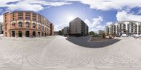 a fisheye view of buildings across a brick plaza in a city, with a sky background