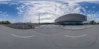 a fish eye lens of a building and parking lot in the distance, with a white sky and clouds overhead