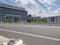 a empty road with a bunch of metal buildings in the background while parked bicycles are parked