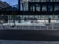 a street has several white concrete poles by it at night, and in the center is some glass, with glass and some greenery in front