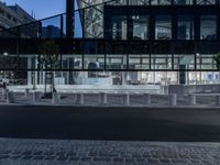 a street has several white concrete poles by it at night, and in the center is some glass, with glass and some greenery in front