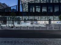 a street has several white concrete poles by it at night, and in the center is some glass, with glass and some greenery in front