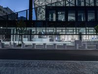 a street has several white concrete poles by it at night, and in the center is some glass, with glass and some greenery in front