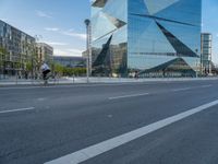 there is a man riding a bike near the side of a building with a glass tower