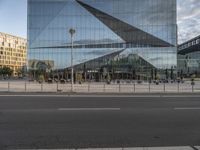 an empty street outside with glass buildings in the background and people walking in front of it