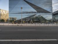 an empty street outside with glass buildings in the background and people walking in front of it