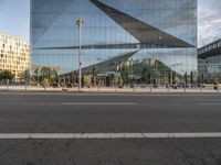 an empty street outside with glass buildings in the background and people walking in front of it