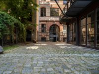 a cobblestone paved patio near an old brick building with two balconies