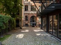 a cobblestone paved patio near an old brick building with two balconies