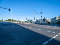 a empty street with buildings in the background on a sunny day and traffic lights illuminating by