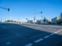 a empty street with buildings in the background on a sunny day and traffic lights illuminating by