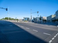 a empty street with buildings in the background on a sunny day and traffic lights illuminating by