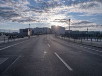 an empty road and some buildings on either side of the river during sunset in daylight