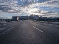 an empty road and some buildings on either side of the river during sunset in daylight