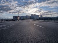 an empty road and some buildings on either side of the river during sunset in daylight