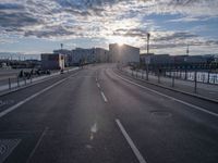 an empty road and some buildings on either side of the river during sunset in daylight