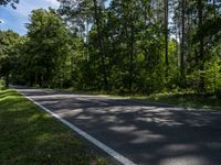 a asphalt road in front of wooded trees and blue sky with fluffy white clouds above