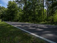 a asphalt road in front of wooded trees and blue sky with fluffy white clouds above