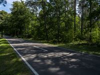 a asphalt road in front of wooded trees and blue sky with fluffy white clouds above