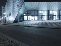 the empty walkway next to a glass structure on a building street in the city at night