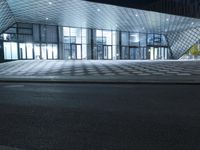 the empty walkway next to a glass structure on a building street in the city at night