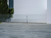 a concrete floor with large tiles outside the building and a fence surrounding it in front of an iron gate