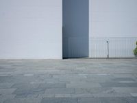 a concrete floor with large tiles outside the building and a fence surrounding it in front of an iron gate