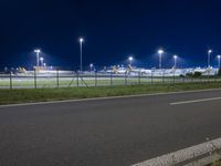 an airport at night with the runway in view, illuminated by street lamps and a fence