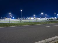 an airport at night with the runway in view, illuminated by street lamps and a fence