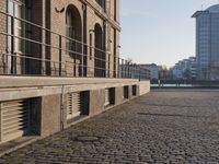 the building is brown brick in the foreground and a sidewalk has cobbles on it
