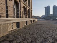 the building is brown brick in the foreground and a sidewalk has cobbles on it