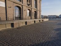 the building is brown brick in the foreground and a sidewalk has cobbles on it