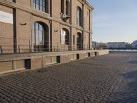 the building is brown brick in the foreground and a sidewalk has cobbles on it