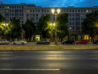 a street in the evening next to trees and a building on the corner with light on the windows