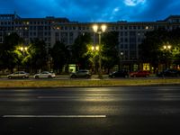 a street in the evening next to trees and a building on the corner with light on the windows