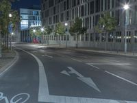 a deserted street with lights shining in the dark and trees and buildings at night with bicycle lane marking