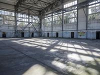 a large empty warehouse is seen with its windows covered in graffiti and shadows on the floor