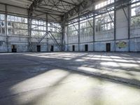 a large empty warehouse is seen with its windows covered in graffiti and shadows on the floor