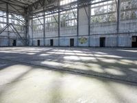 a large empty warehouse is seen with its windows covered in graffiti and shadows on the floor