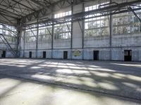 a large empty warehouse is seen with its windows covered in graffiti and shadows on the floor