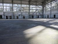 a large empty warehouse is seen with its windows covered in graffiti and shadows on the floor