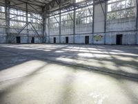 a large empty warehouse is seen with its windows covered in graffiti and shadows on the floor