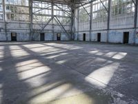 a large empty warehouse is seen with its windows covered in graffiti and shadows on the floor