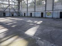 a large empty warehouse is seen with its windows covered in graffiti and shadows on the floor