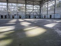 a large empty warehouse is seen with its windows covered in graffiti and shadows on the floor